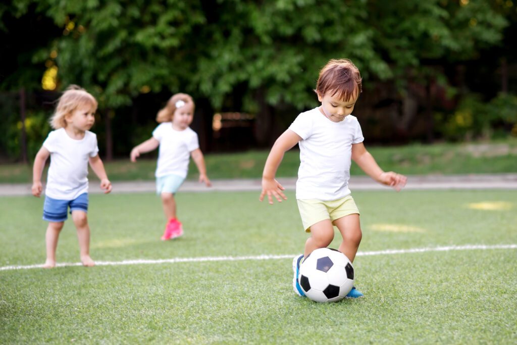 Football Game Team Of Toddlers Playing Soccer On Green Field